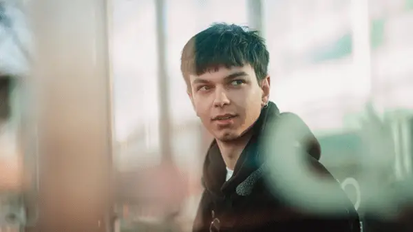 A seated young adult male wearing a black hoody - this image also features on the cover of the report entitled The Youth Penalty